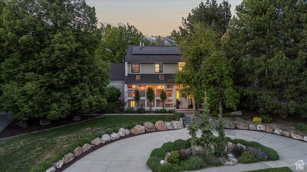 Back of property at dusk with a porch, roof mounted solar panels, and a lawn