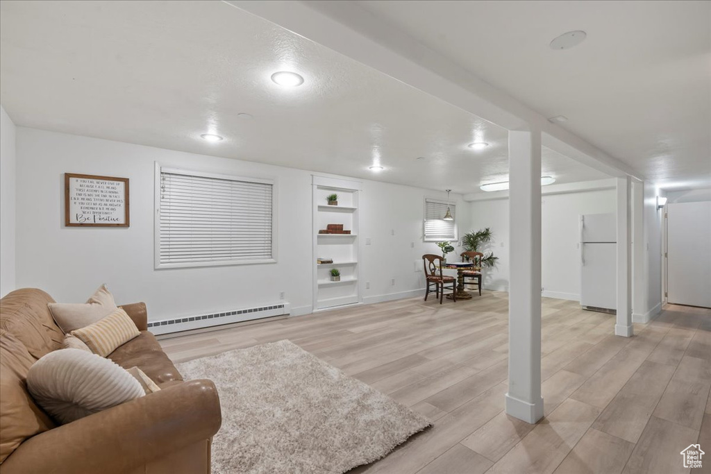 Living room featuring baseboard heating, built in shelves, baseboards, and light wood-type flooring