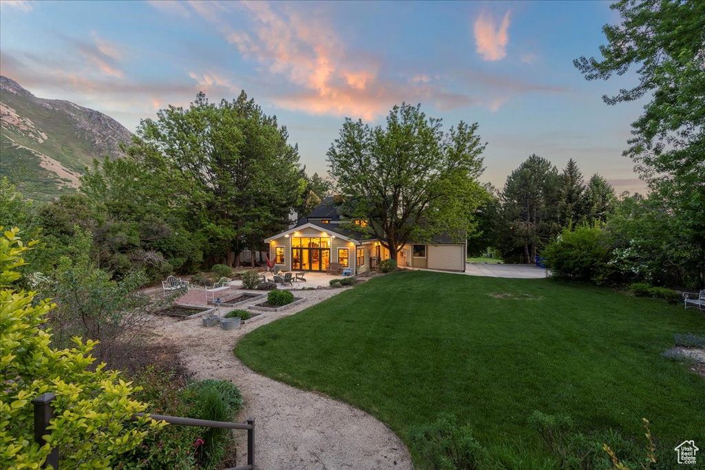 View of green lawn with a patio, a vegetable garden, driveway, and a mountain view
