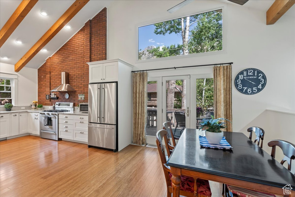 Kitchen featuring high end appliances, high vaulted ceiling, wall chimney range hood, beam ceiling, and white cabinets