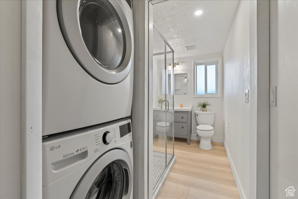 Laundry room with stacked washer / drying machine, light wood-style floors, and baseboards