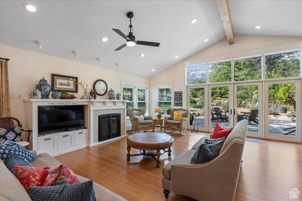 Living room featuring beamed ceiling, wood finished floors, ceiling fan, a glass covered fireplace, and high vaulted ceiling