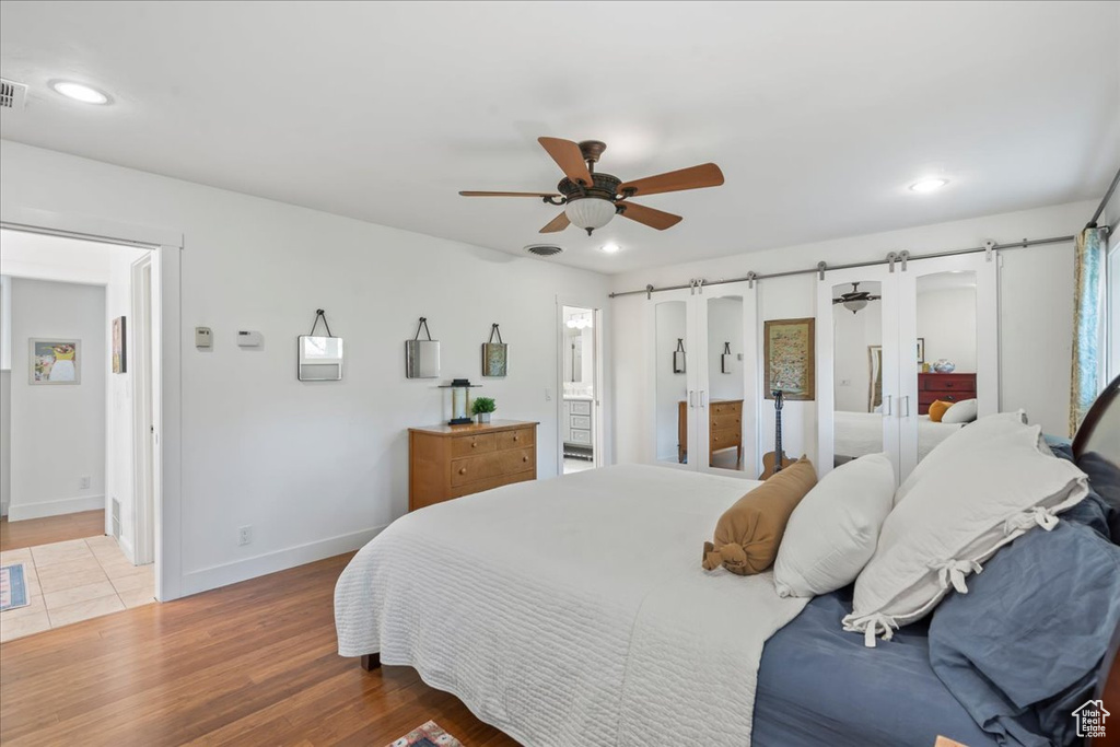 Bedroom featuring a barn door, connected bathroom, wood finished floors, recessed lighting, and baseboards