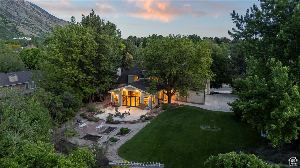 Back of house at dusk with a patio area and a lawn
