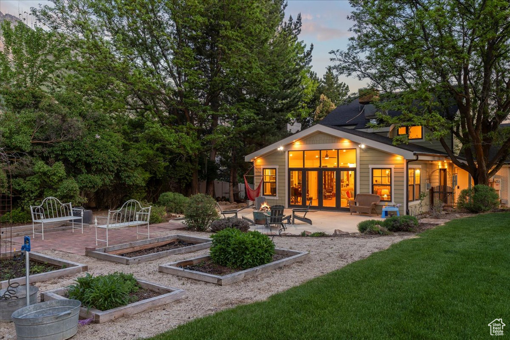 Back of property at dusk with a vegetable garden, a patio area, an outdoor fire pit, and a lawn