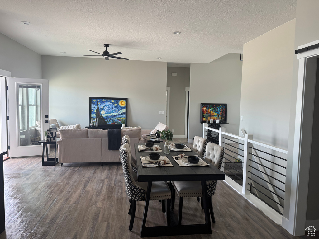 Dining space with dark wood-style floors, ceiling fan, a textured ceiling, and a barn door