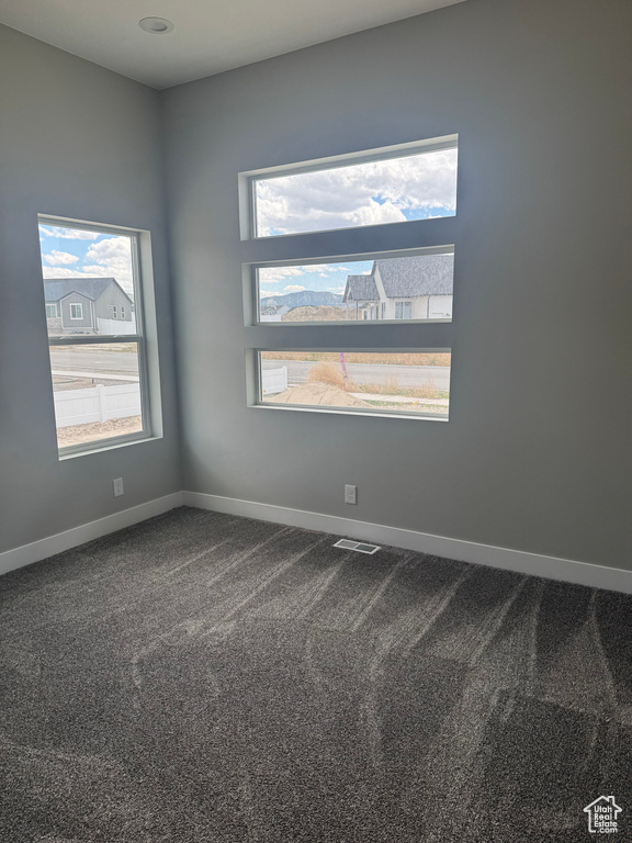 Unfurnished room with plenty of natural light, dark carpet, and baseboards