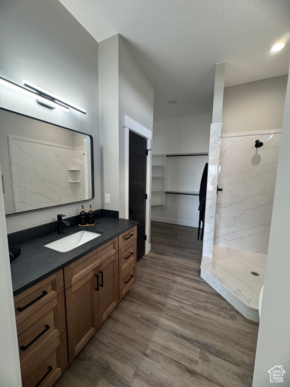 Full bath with a marble finish shower, vanity, wood finished floors, and a textured ceiling