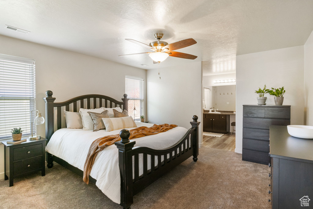 Bedroom featuring light carpet, ensuite bathroom, and a ceiling fan