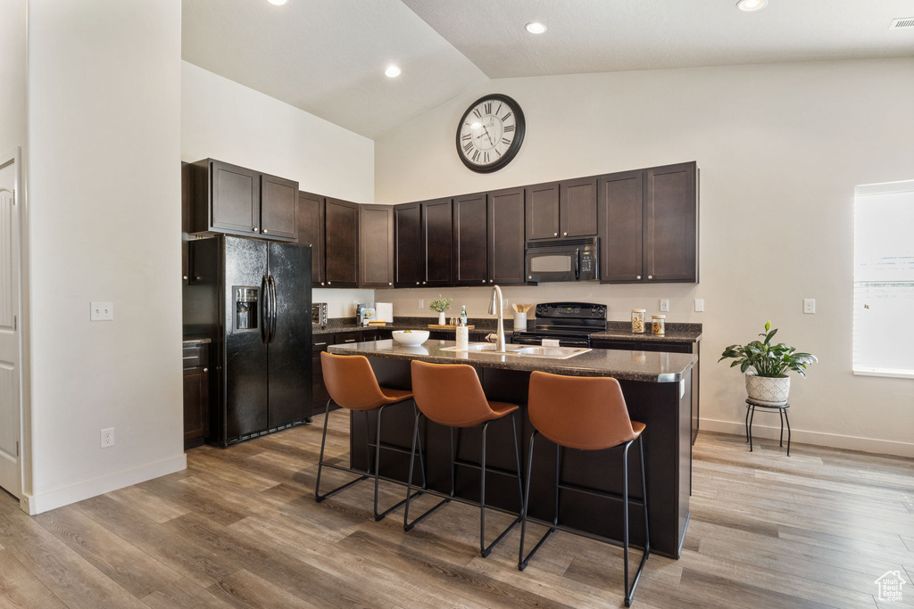 Kitchen with black appliances, high vaulted ceiling, a kitchen bar, an island with sink, and dark brown cabinetry
