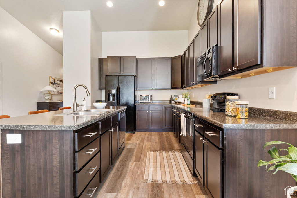 Kitchen featuring black appliances, a sink, dark brown cabinetry, and light wood finished floors