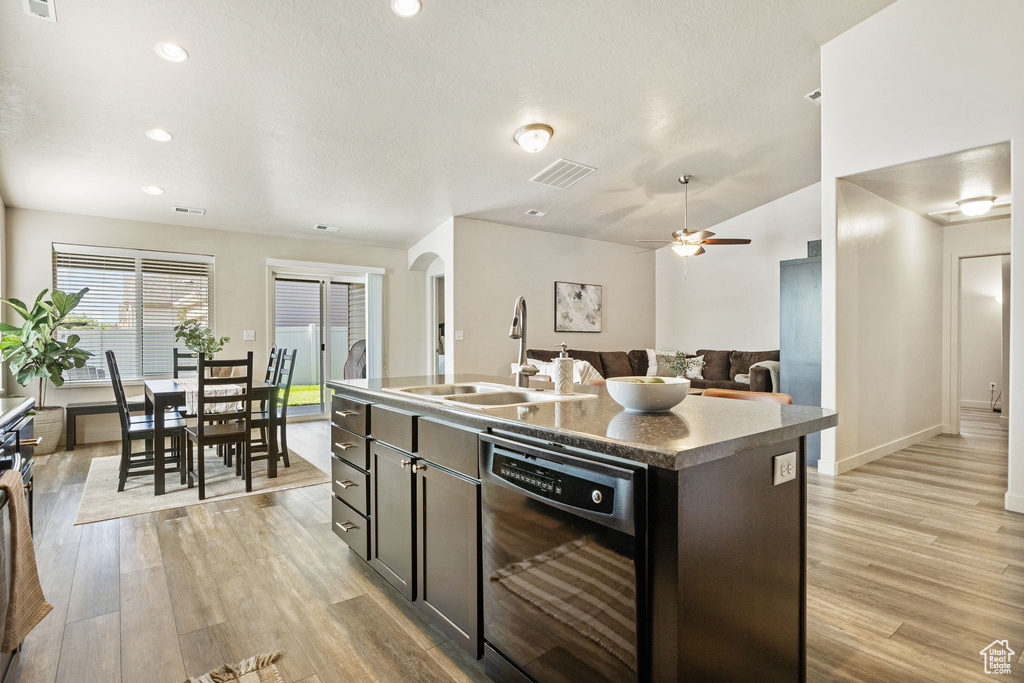 Kitchen with black dishwasher, a sink, light wood-type flooring, arched walkways, and a center island with sink