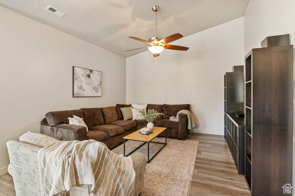 Living room with light wood-style flooring, a ceiling fan, baseboards, and lofted ceiling