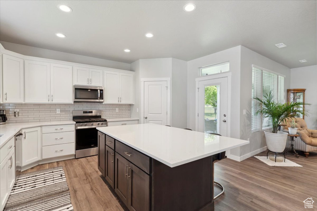 Kitchen with stainless steel appliances, light wood-style floors, white cabinetry, light countertops, and decorative backsplash