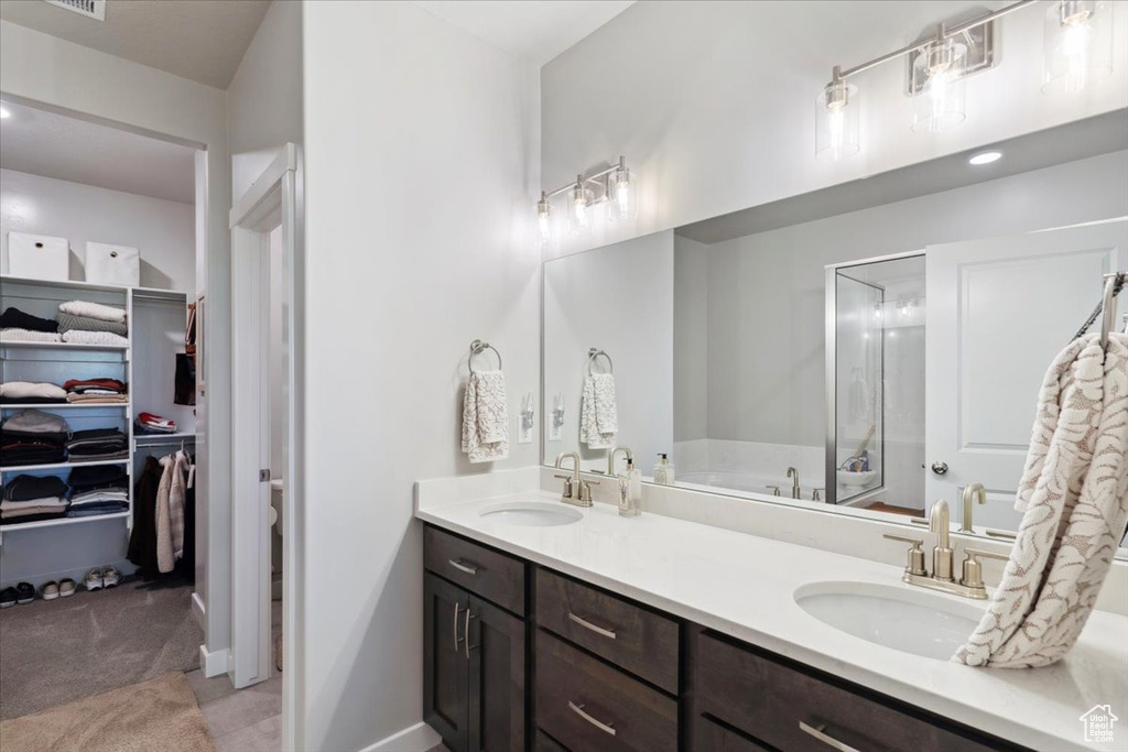 Full bath featuring double vanity, a bath, a shower stall, a walk in closet, and baseboards