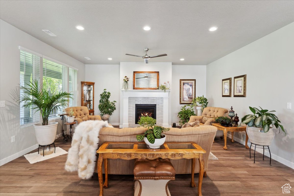 Living room with baseboards, wood finished floors, recessed lighting, a brick fireplace, and ceiling fan