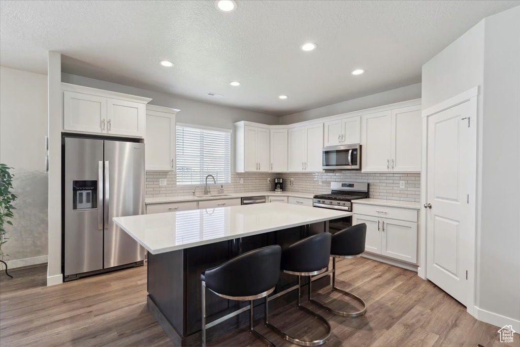 Kitchen featuring appliances with stainless steel finishes, a sink, a center island, white cabinets, and backsplash