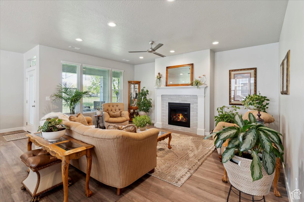 Living room featuring a ceiling fan, a brick fireplace, wood finished floors, recessed lighting, and baseboards