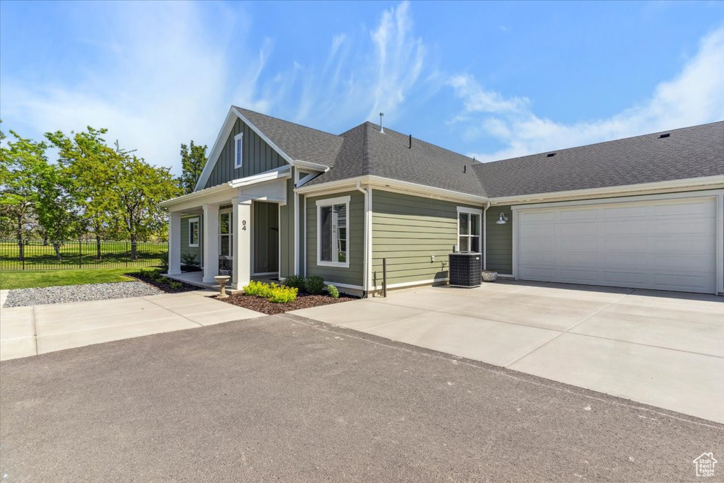 View of front facade featuring concrete driveway, a garage, roof with shingles, central AC, and board and batten siding