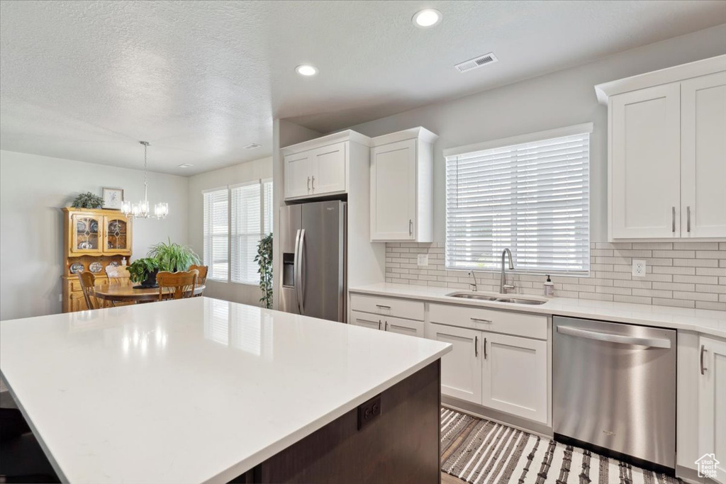 Kitchen with stainless steel appliances, a sink, decorative backsplash, light countertops, and white cabinetry