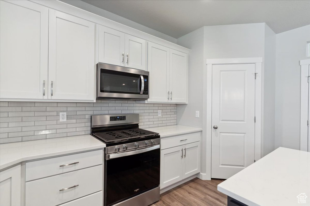 Kitchen featuring stainless steel appliances, light wood-type flooring, white cabinets, and tasteful backsplash