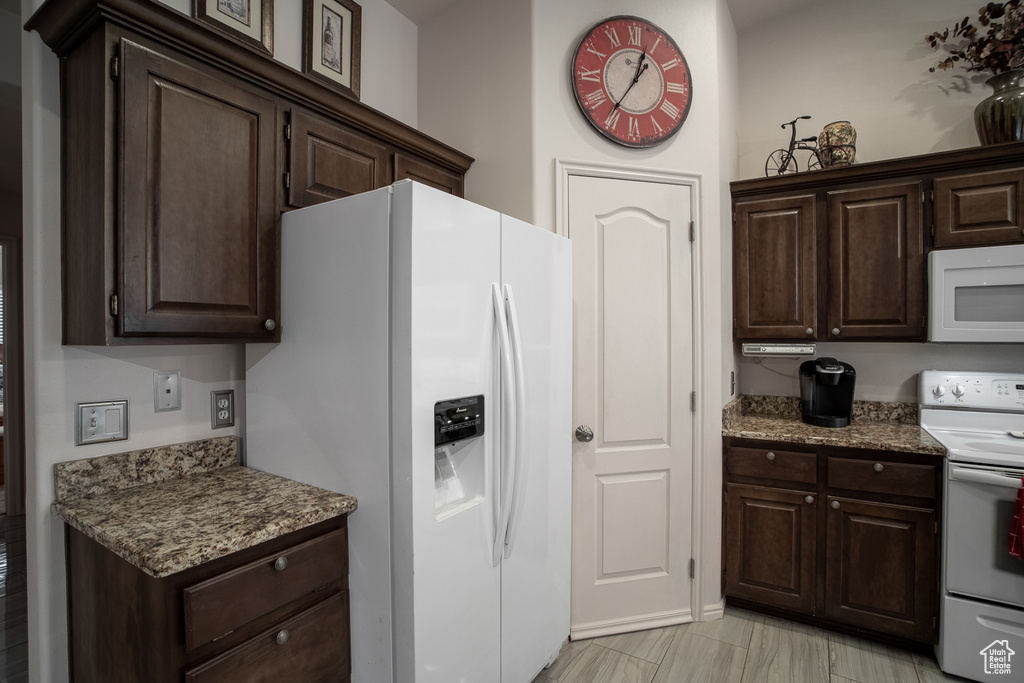 Kitchen featuring white appliances, dark brown cabinetry, and stone counters