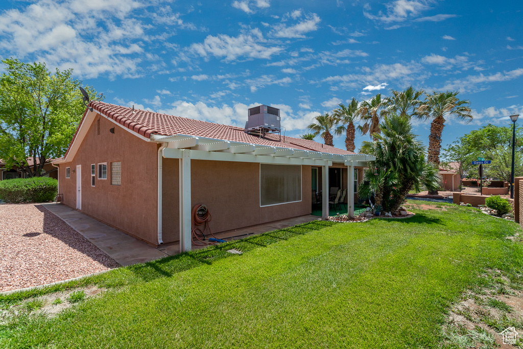 Rear view of property featuring central AC, a yard, a tile roof, and stucco siding