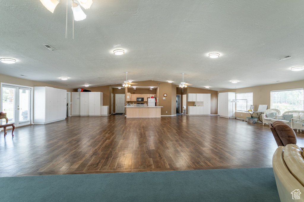 Living room featuring ceiling fan, dark wood-type flooring, lofted ceiling, a textured ceiling, and baseboards