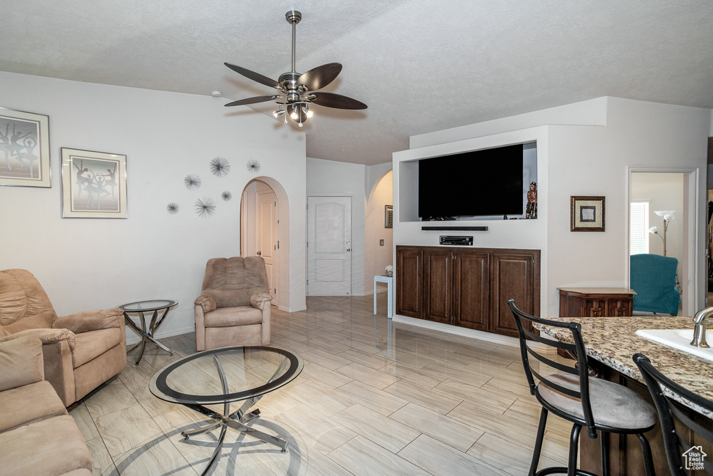 Living room featuring arched walkways, a ceiling fan, a textured ceiling, and baseboards