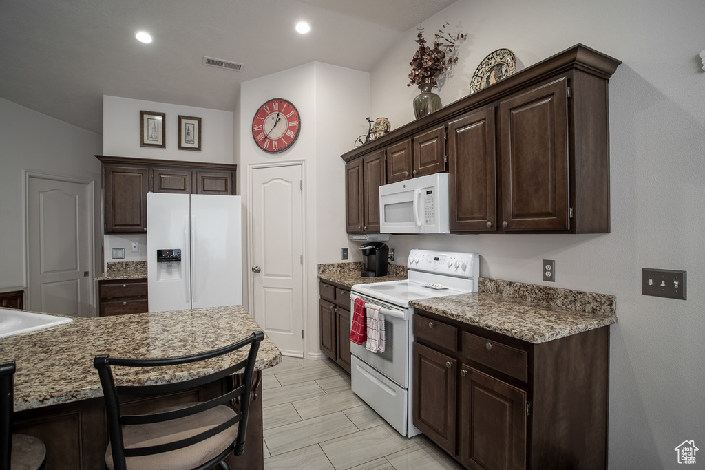 Kitchen with white appliances, dark brown cabinets, recessed lighting, and a kitchen breakfast bar