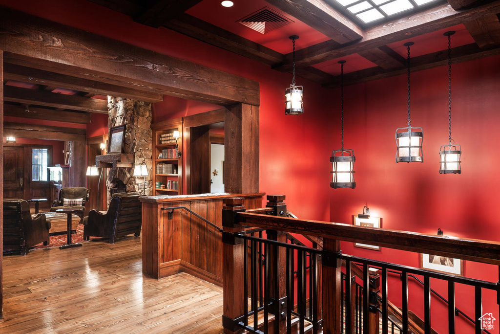 Bar area with beamed ceiling, hardwood / wood-style flooring, coffered ceiling, and a stone fireplace