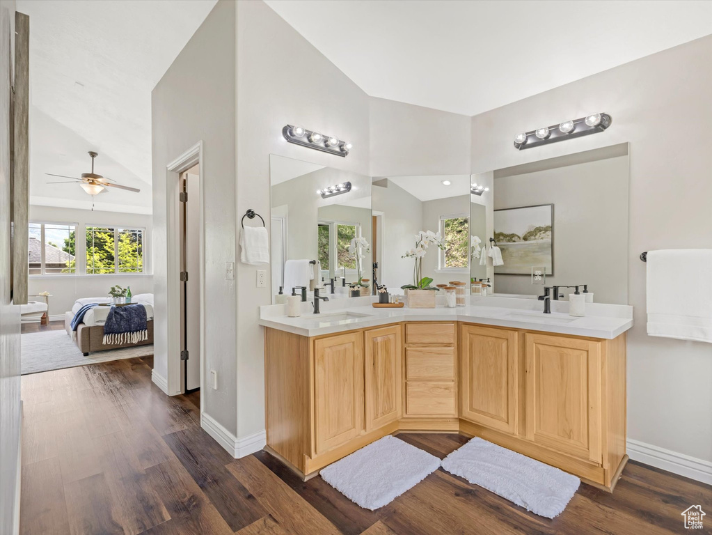 Ensuite bathroom with double vanity, wood finished floors, lofted ceiling, a ceiling fan, and baseboards