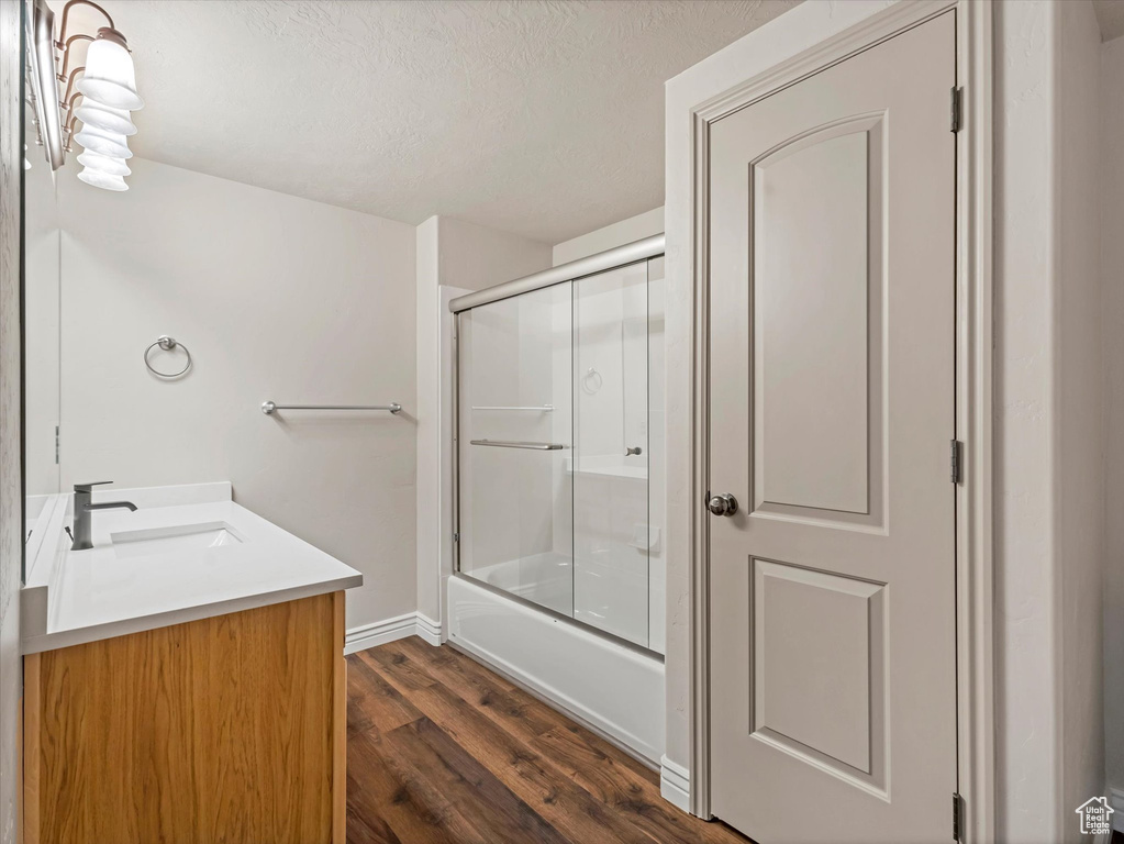 Full bathroom featuring vanity, wood finished floors, bath / shower combo with glass door, a textured ceiling, and baseboards
