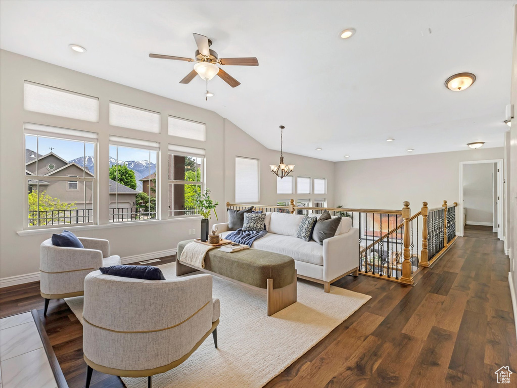 Living room with ceiling fan, a chandelier, dark wood-type flooring, vaulted ceiling, and baseboards