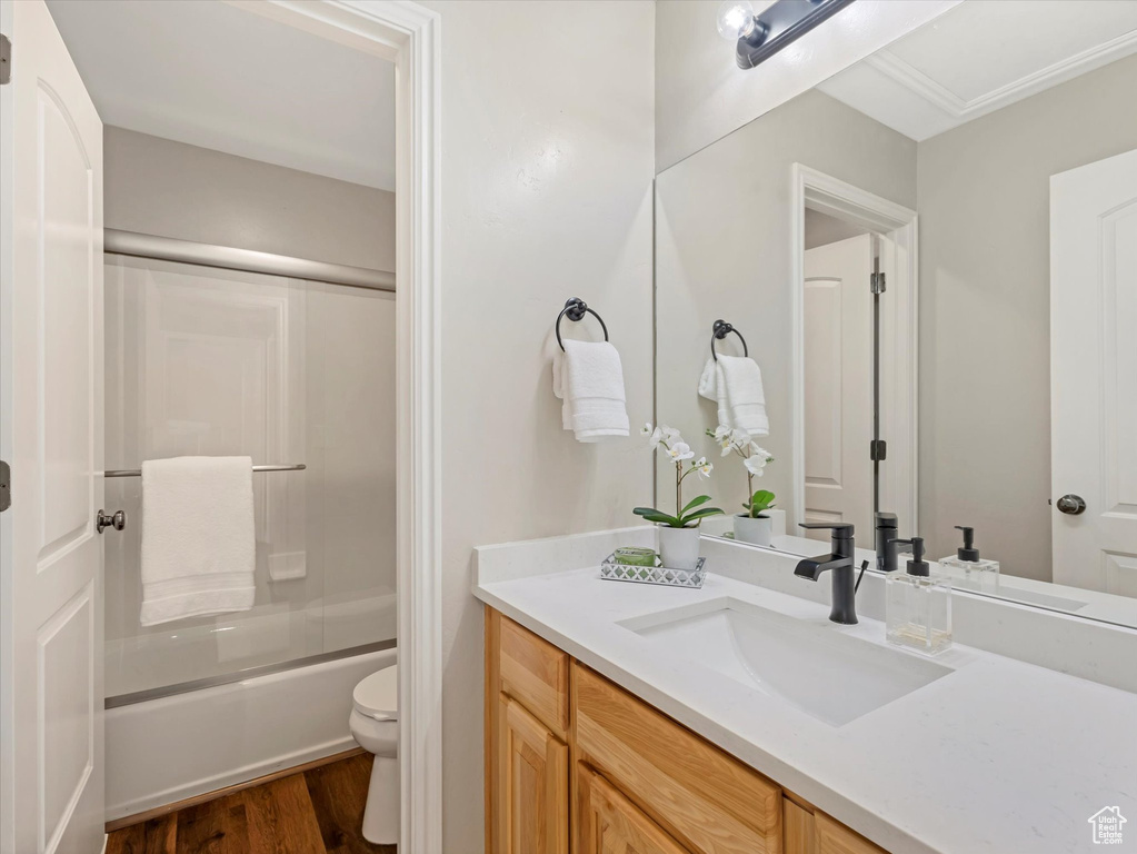Bathroom with vanity, toilet, wood finished floors, and shower / bath combination with glass door