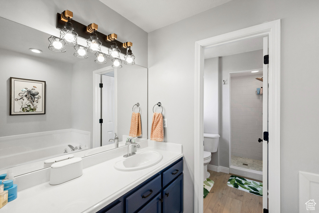 Bathroom featuring toilet, wood finished floors, vanity, tiled shower, and baseboards