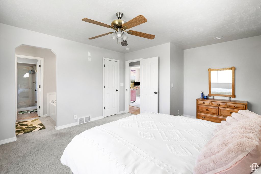 Bedroom with light colored carpet, baseboards, arched walkways, a ceiling fan, and ensuite bath