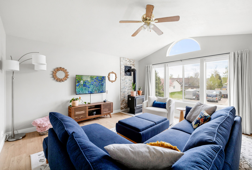 Living area featuring a wood stove, vaulted ceiling, a ceiling fan, light wood-type flooring, and baseboards