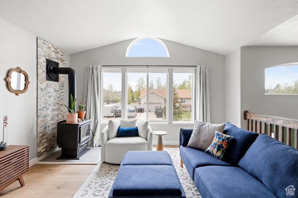 Living room with a wood stove, light wood-style floors, and vaulted ceiling