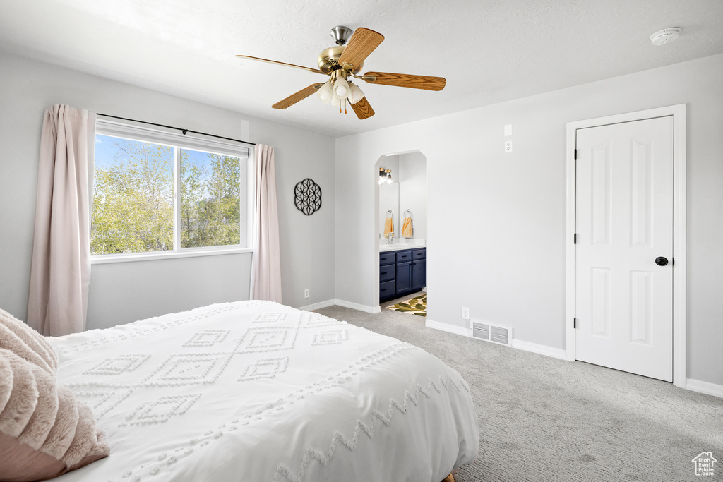 Bedroom featuring light colored carpet, baseboards, ensuite bathroom, and ceiling fan