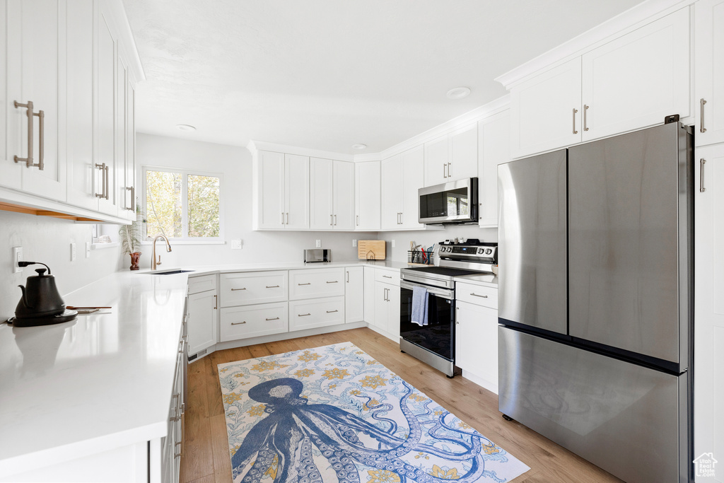 Kitchen with stainless steel appliances, light wood-style floors, white cabinets, and a sink