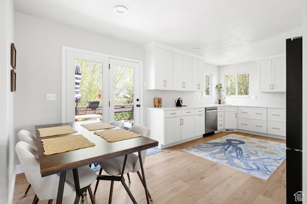 Kitchen with dishwasher, black fridge, light wood-style floors, a sink, and white cabinets
