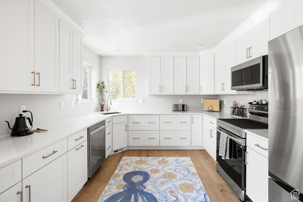 Kitchen featuring appliances with stainless steel finishes, a sink, white cabinets, and light wood finished floors