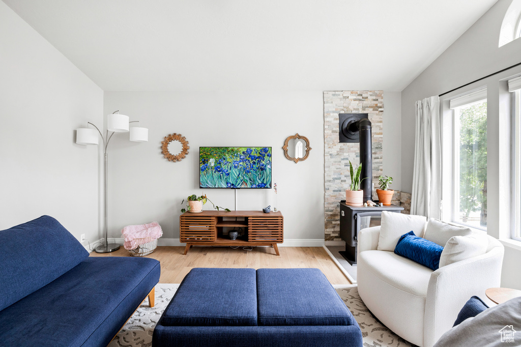 Living room featuring a wood stove, light wood-style floors, lofted ceiling, and baseboards