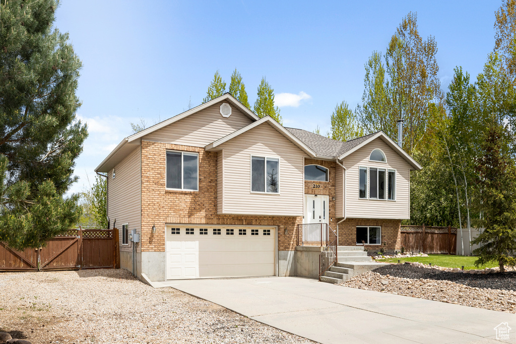 Raised ranch with a garage, driveway, a gate, and brick siding