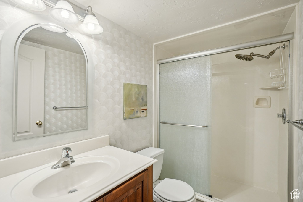 Full bathroom featuring wallpapered walls, a shower stall, vanity, toilet, and a textured ceiling
