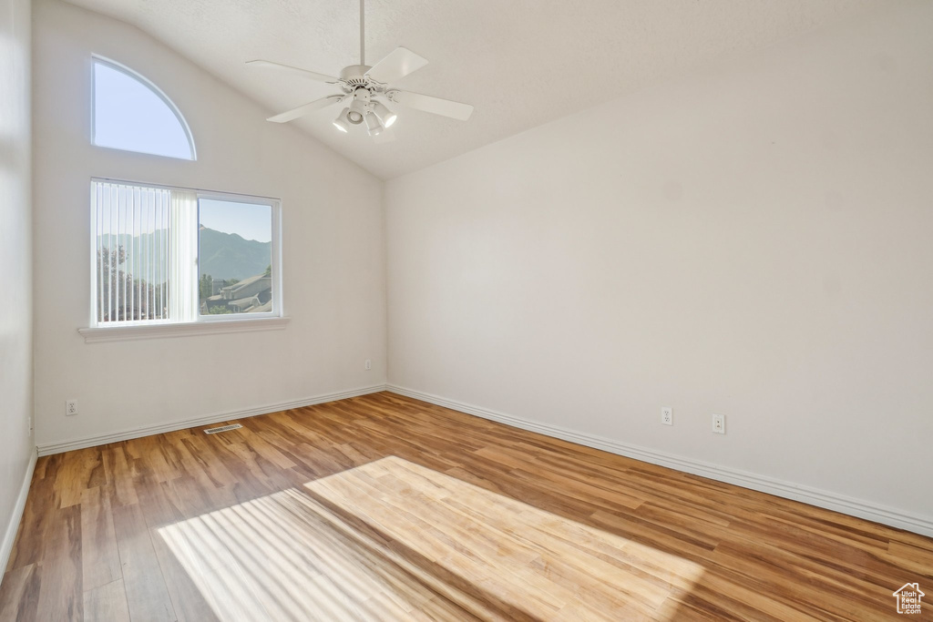 Empty room with wood finished floors, vaulted ceiling, a ceiling fan, and baseboards