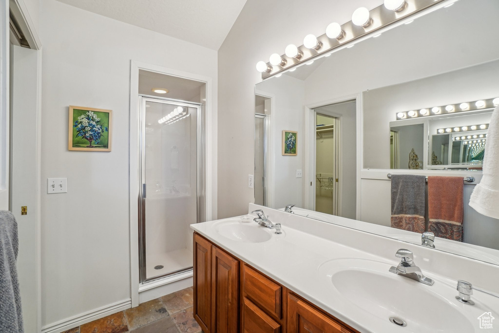 Full bath featuring a stall shower, double vanity, a spacious closet, and stone finish floors