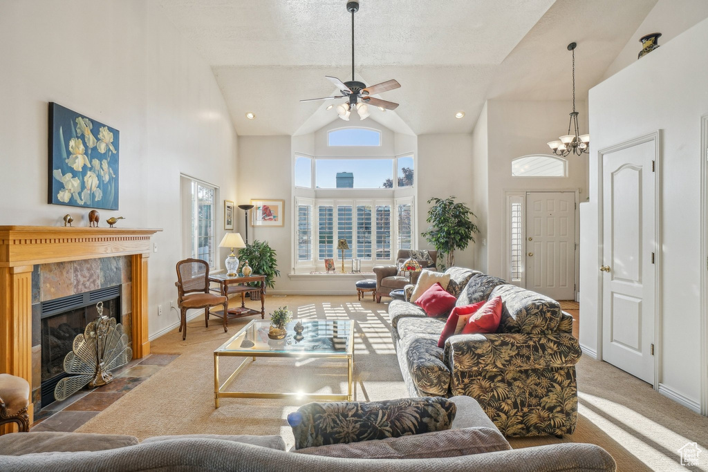 Living room with high vaulted ceiling, a tile fireplace, ceiling fan, baseboards, and a chandelier