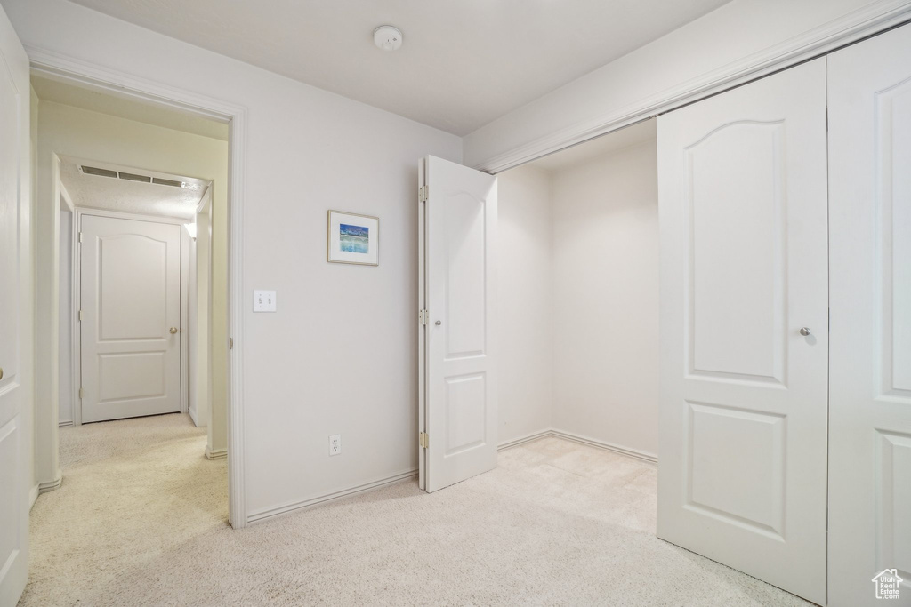 Unfurnished bedroom with light carpet, a closet, and baseboards